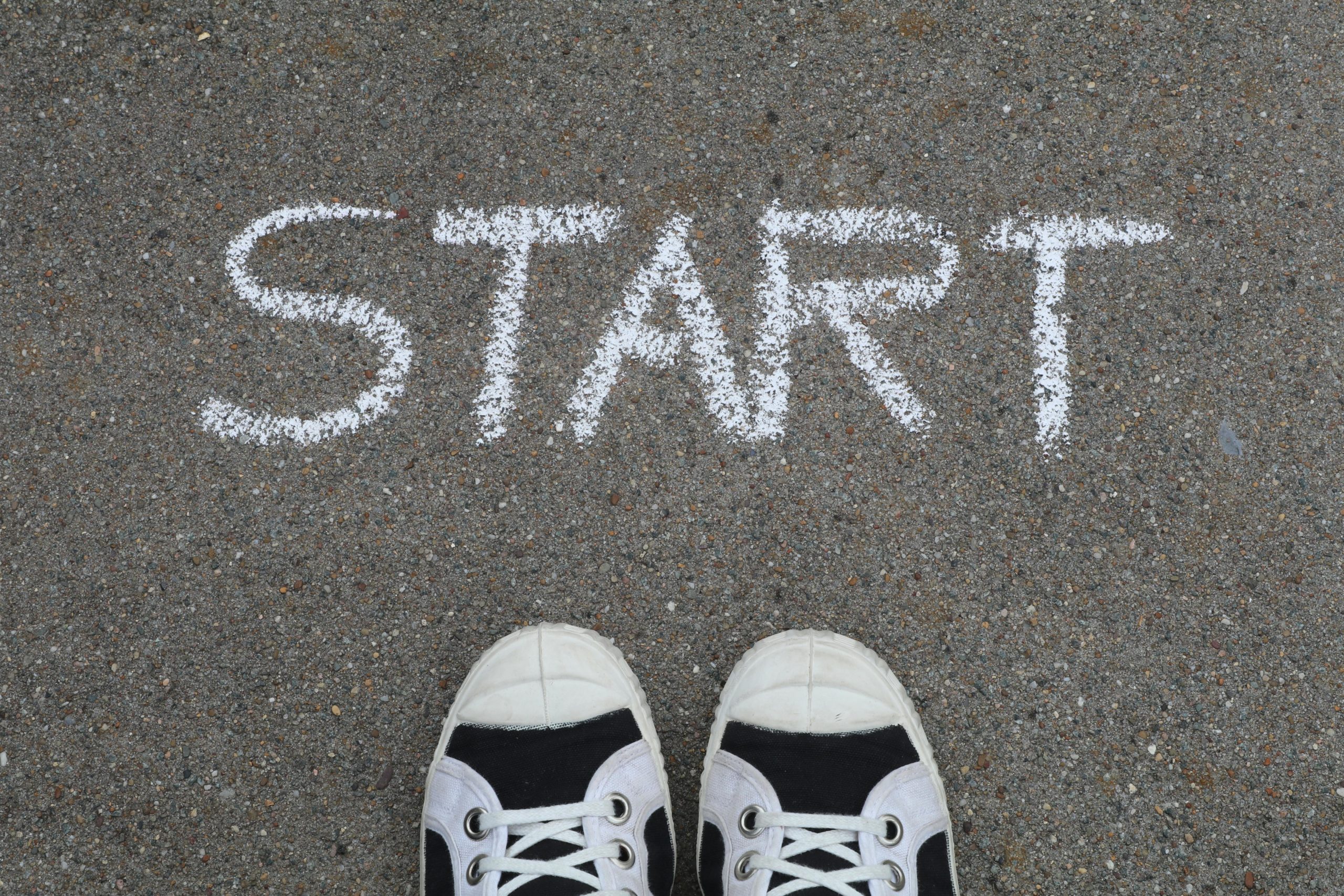 START written in chalk in front of the toes of a pair of plimsoles