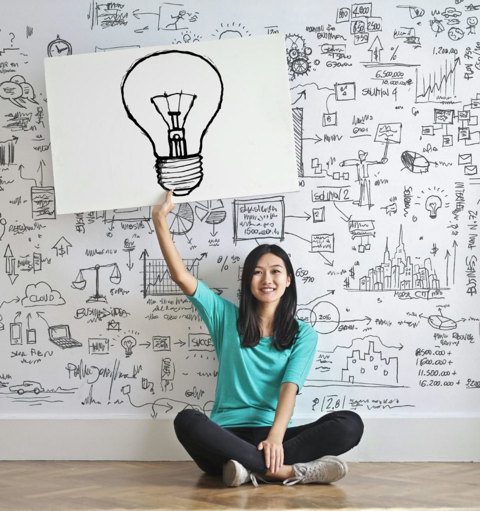 Happy woman sat cross legged on the floor holding up picture of a lightbulb